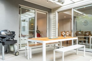 Eine Terrasse im Freien mit einem Grill, einem Holztisch und einer Bank.