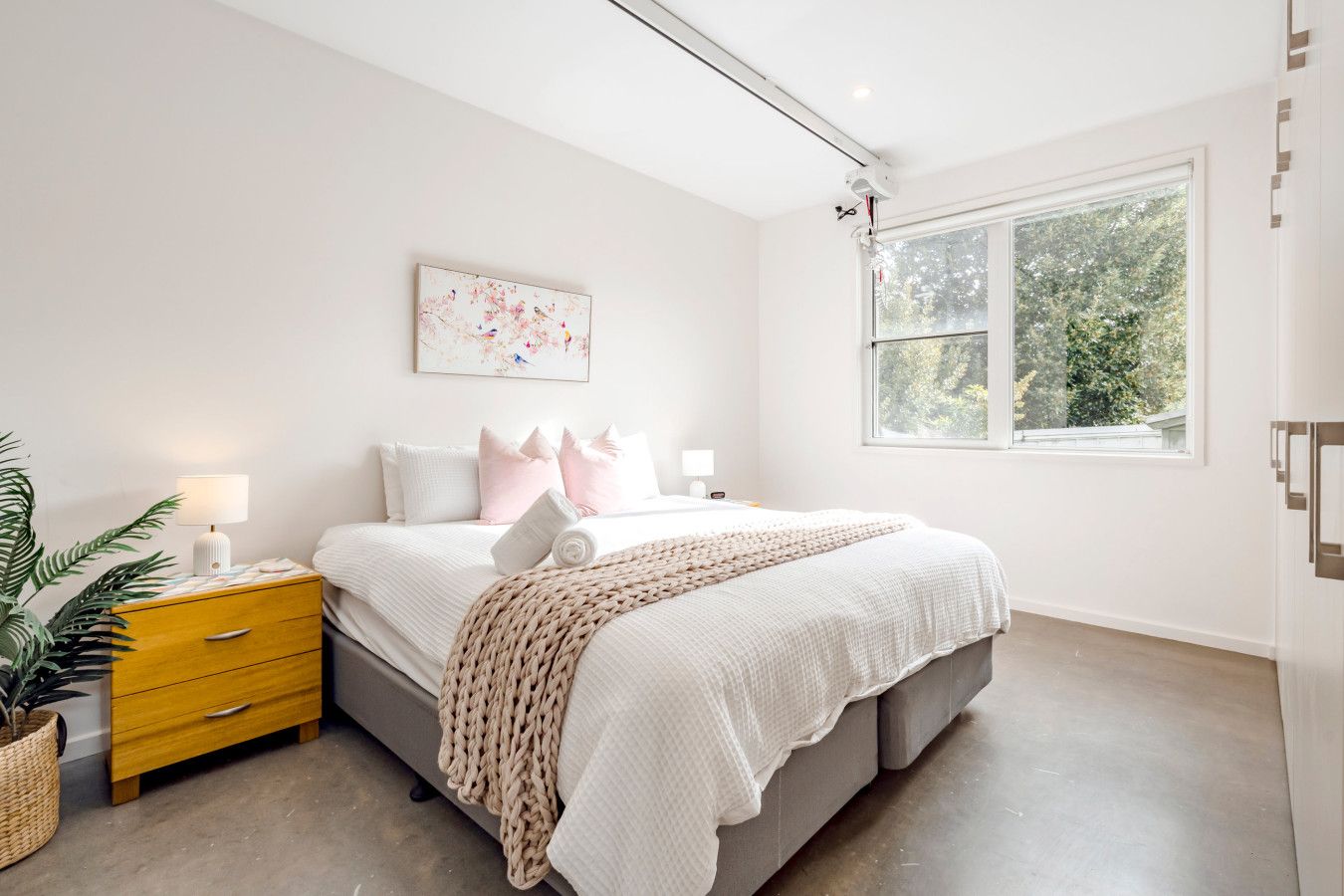 Ein modernes Schlafzimmer mit Bett, Nachttischen, einem Fenster und einer Pflanze.