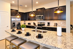 A modern kitchen with dark cabinets, granite countertops, stainless steel appliances, and pendant lighting. - Windsor Island 5BR with Pool & Waterpark (Davenport)