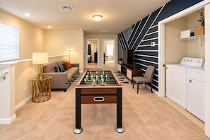 A room with a foosball table, a sofa, a lamp, and a washing machine. - Windsor Island 5BR with Pool & Waterpark (Davenport)