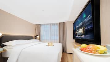 Una habitación de hotel con cama, televisión, mesita de noche, ventana con cortinas y un frutero sobre la cómoda.