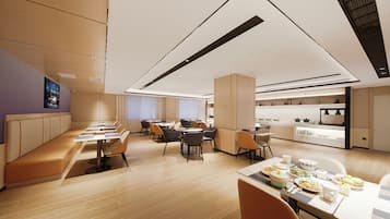 Un espace de restauration moderne avec de longues tables et des bancs, une cuisine à l’arrière-plan et un plafond haut doté d’un éclairage encastré.