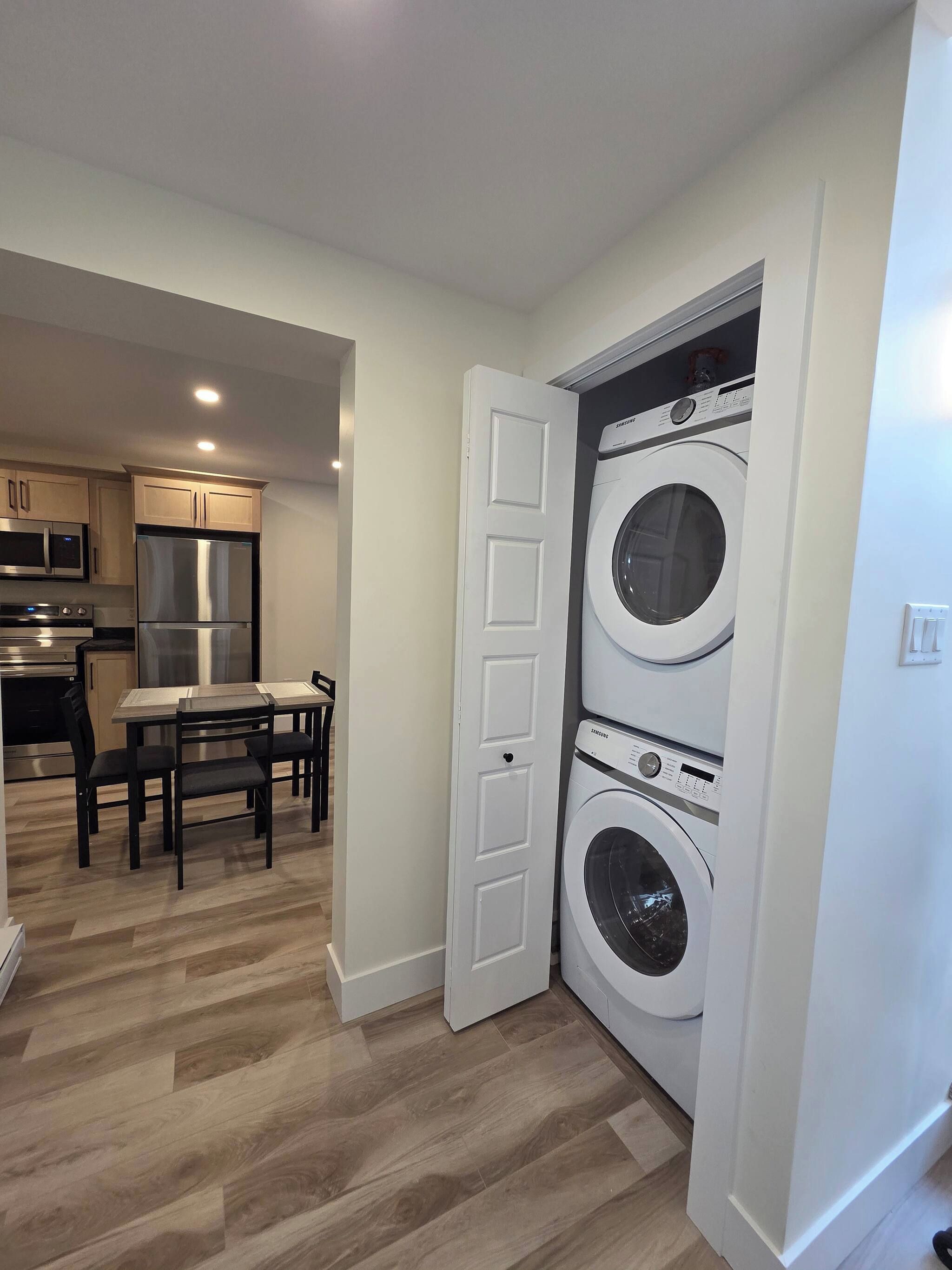 A compact kitchen with modern appliances, a dining area with a table and chairs, and a laundry room with two stacked washing machines.