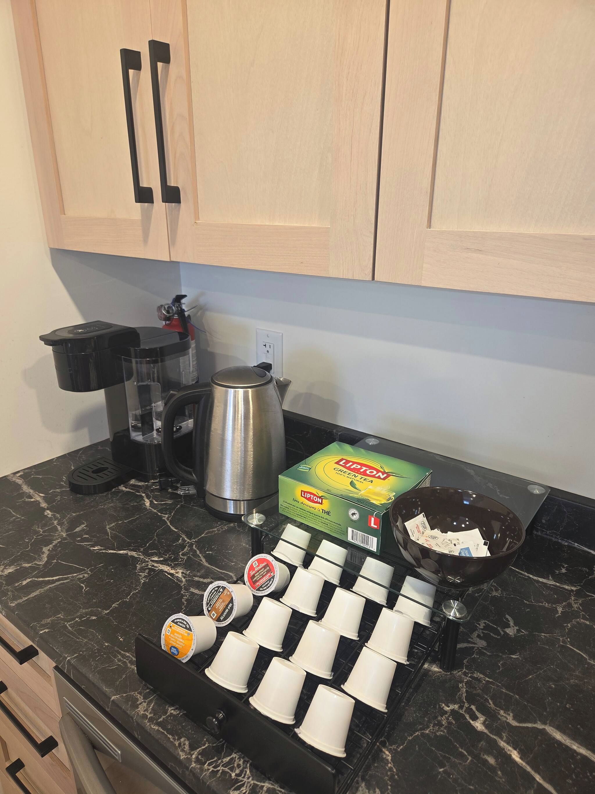 A kitchen counter with a coffee machine, a kettle, Lipton tea boxes, and a tray of disposable cups.