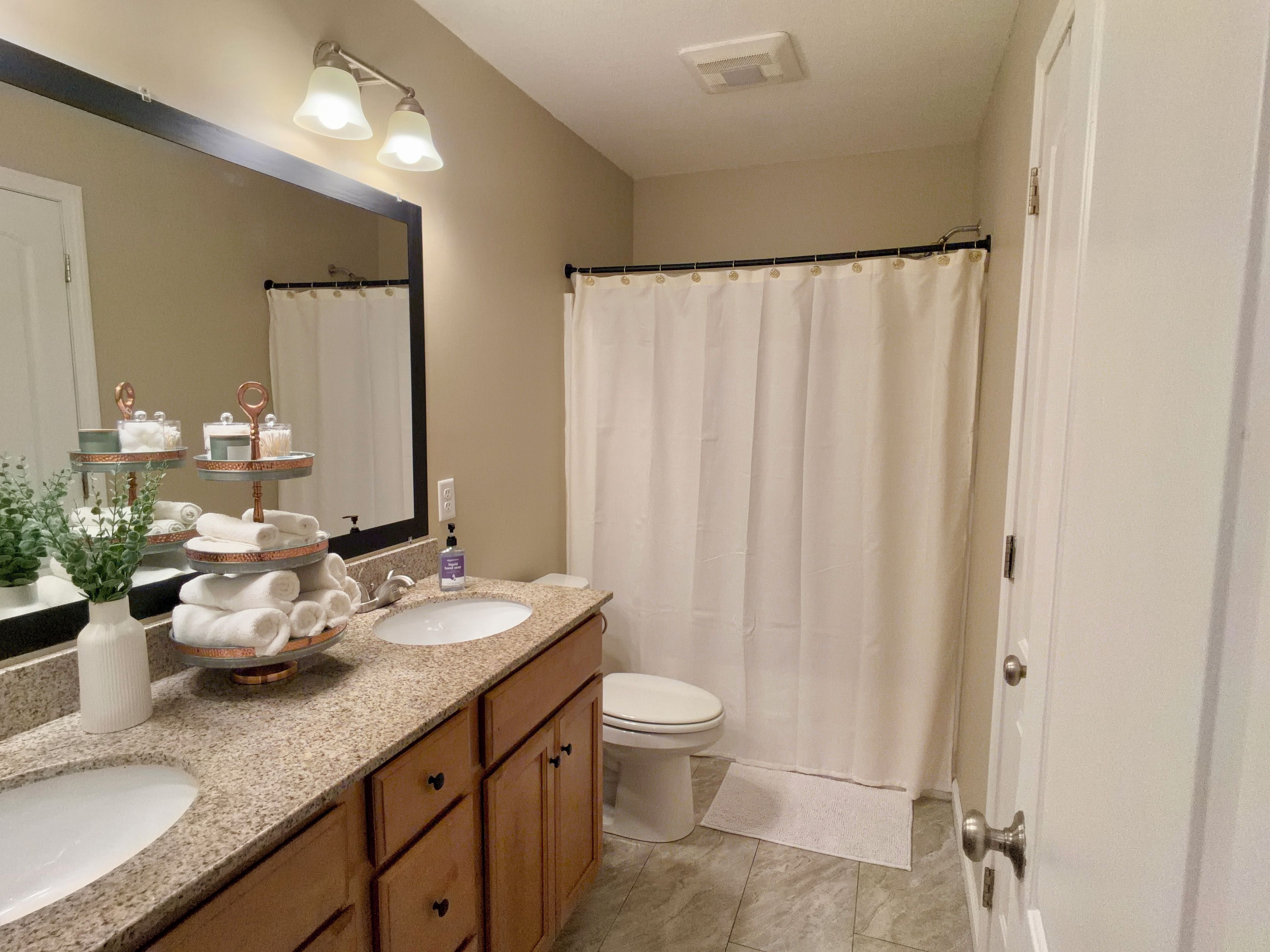 Une salle de bain avec deux lavabos, des toilettes, un rideau de douche et un miroir avec éclairage intégré.