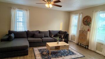 A living room with a sectional sofa, a coffee table, a rug, a ceiling fan, and a clock on the wall.