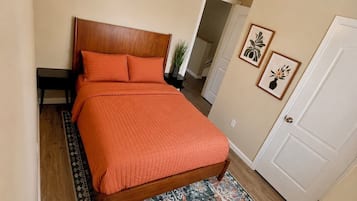 A neatly made bed with a wooden headboard, a small bedside table, and a patterned rug on a wooden floor.