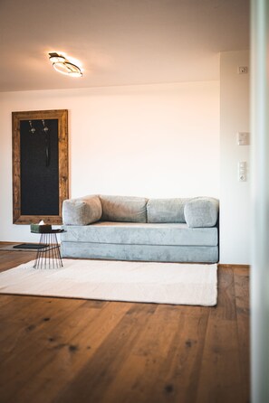 Ett minimalistiskt vardagsrum med en ljusblå soffa, ett litet sidobord och ett trägolv.