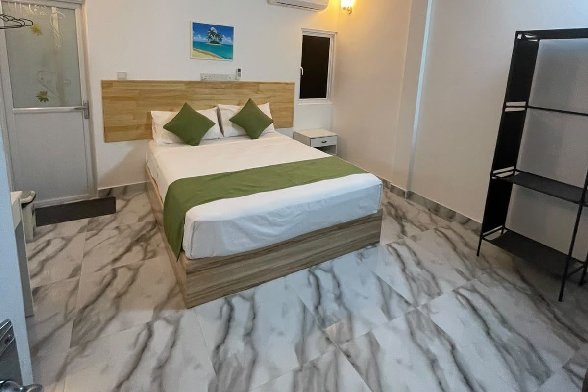 A hotel room with a bed, a ceiling fan, an air conditioning unit, a nightstand, and a shelf.