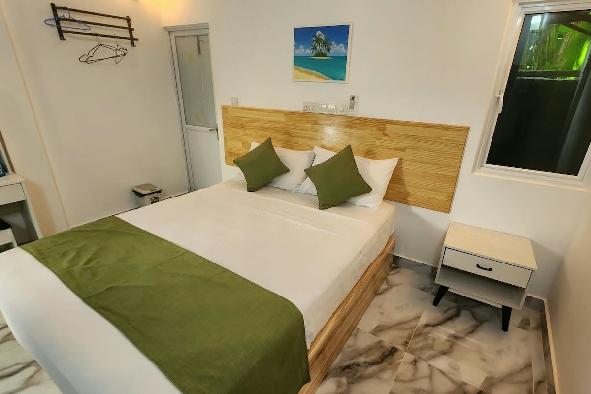 A hotel room with a bed, a nightstand, a desk, and a window.