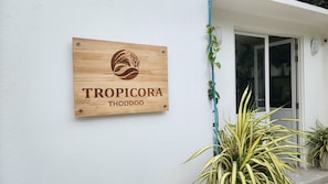 A wooden sign with the name 'TROPICORA THODDOO' mounted on a white wall. - Tropicora Thoddoo (Thoddoo)