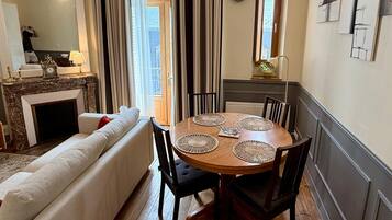 A cozy living room with a fireplace, a dining table with placemats, and a view through a window.