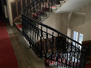 A staircase with ornate black railings, wooden steps, and a red carpet. - Town Centre Apartment, Mont-dore (Mont-Dore)