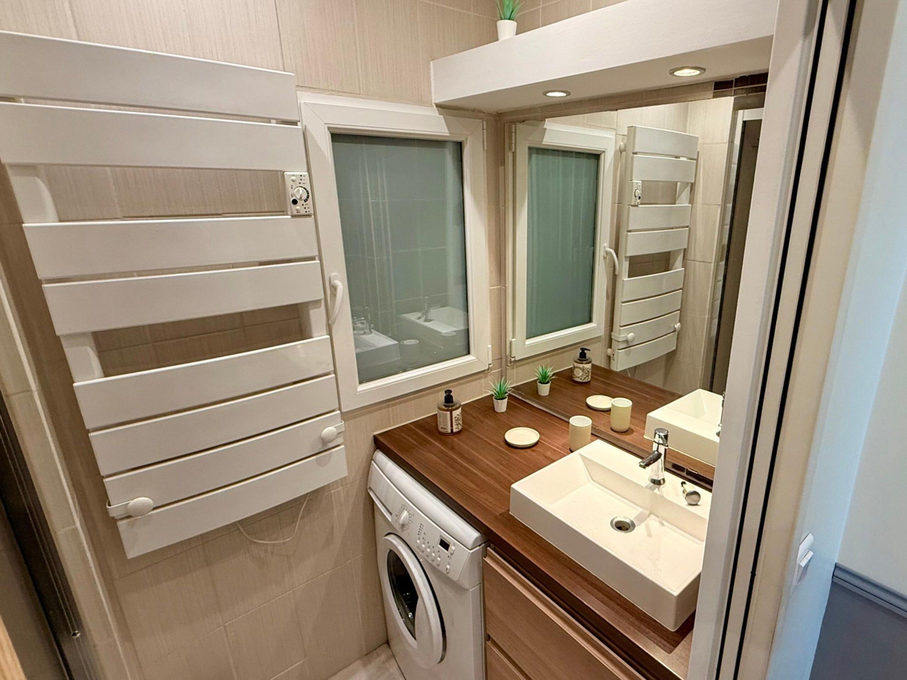 A compact bathroom with a washing machine, a sink, and a mirror.