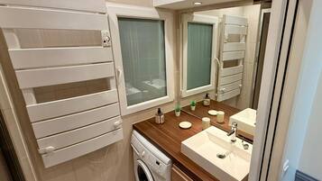 A compact bathroom with a washing machine, a sink, and a mirror.
