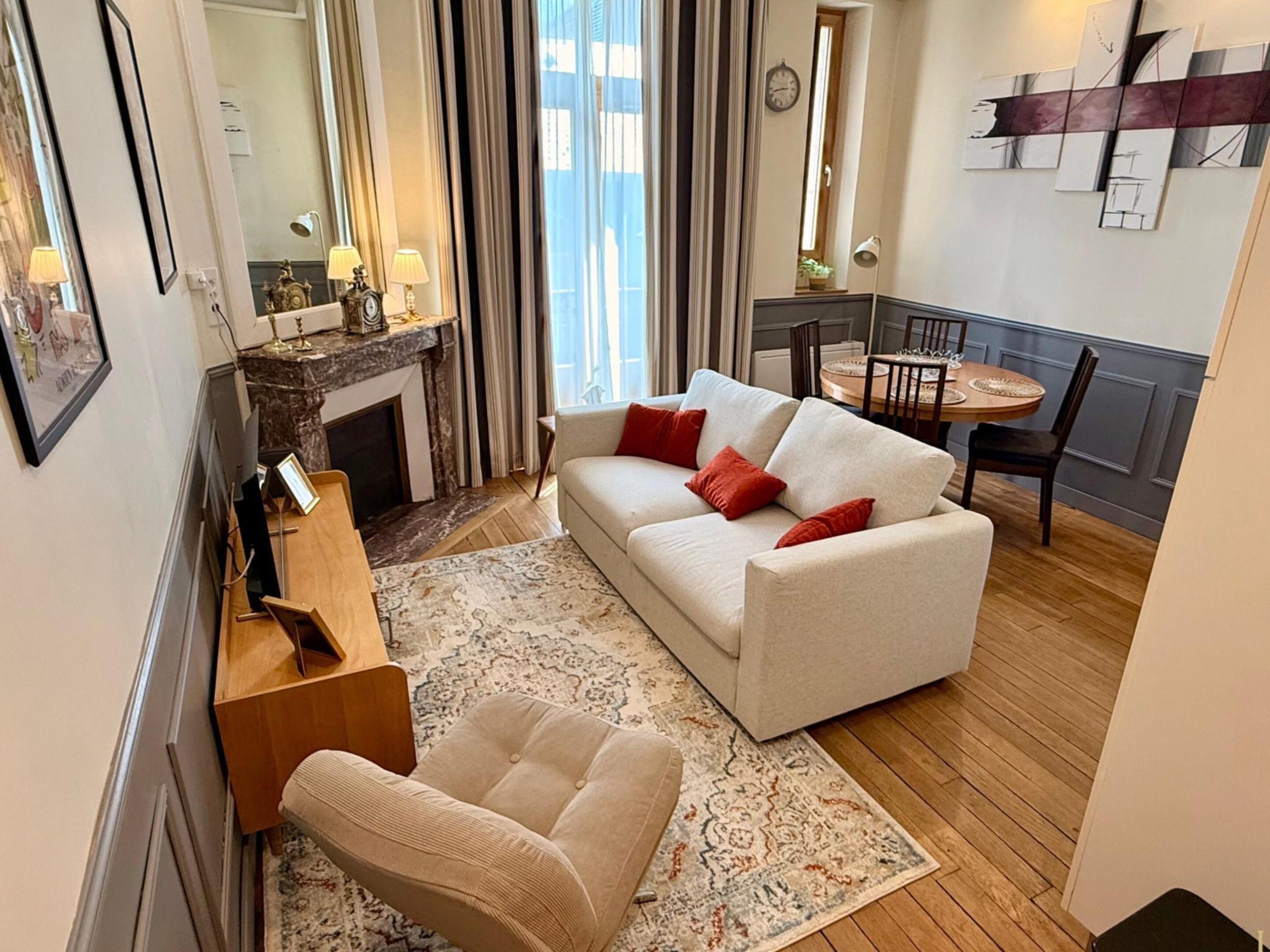 A living room with a sofa, armchair, and a fireplace. There is a dining area with a table and chairs.