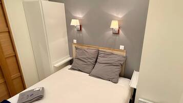 A hotel room with a bed, two bedside lamps, a heater, and a folded towel on the bed.