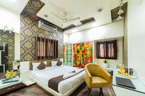 A hotel room with a bed, a desk with a laptop, a chair, a mirror, and a ceiling fan. - Coliwo Deux Hostel - Chandan Nagar (Pune)