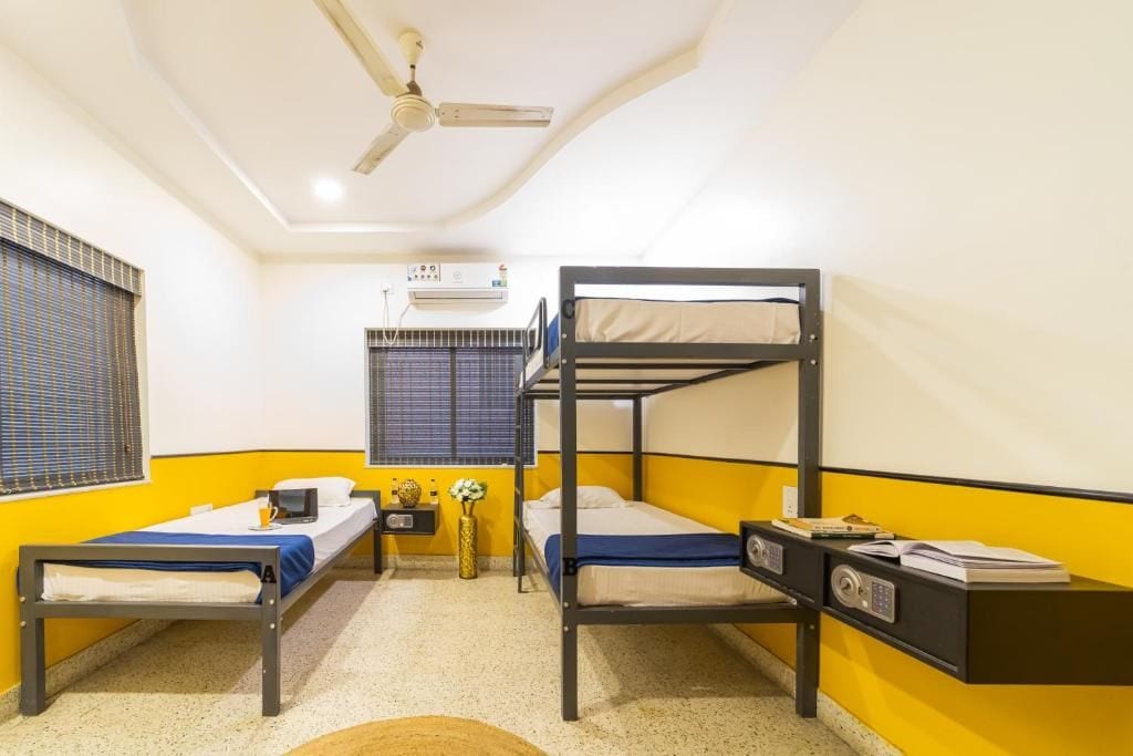 A room with two bunk beds, a ceiling fan, an air conditioning unit, and a small bedside table with a lamp.