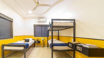 A room with two bunk beds, a ceiling fan, an air conditioning unit, and a small bedside table with a lamp.