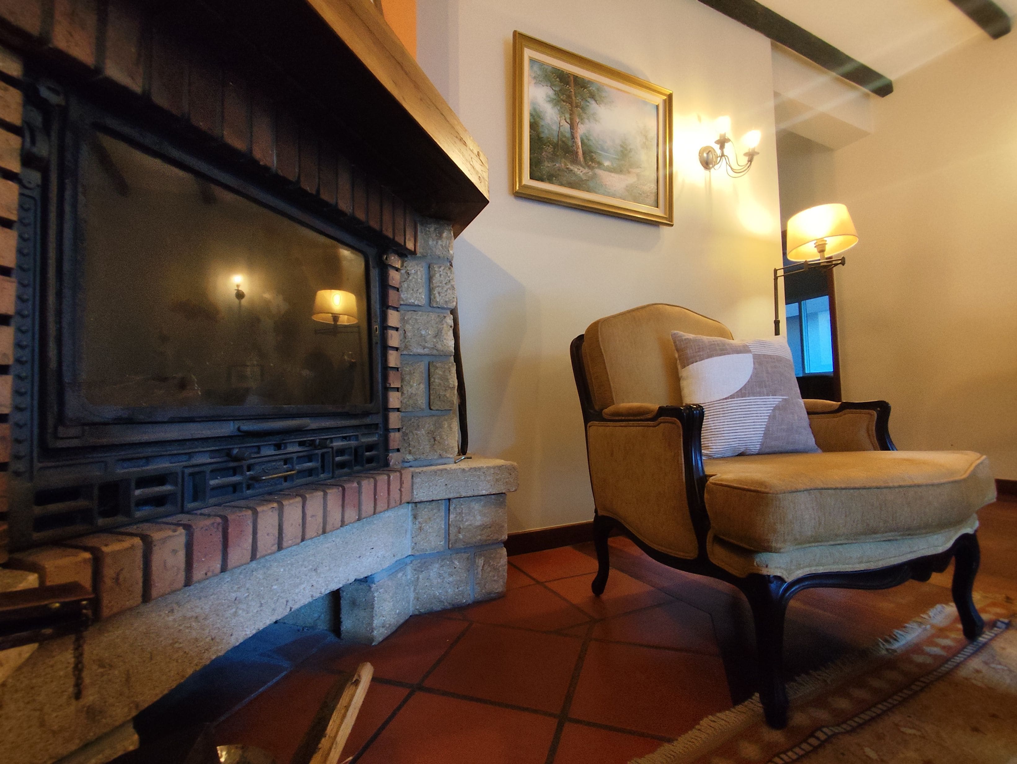 Lareira com revestimento de pedra, um quadro emoldurado na parede e uma cadeira com almofada.