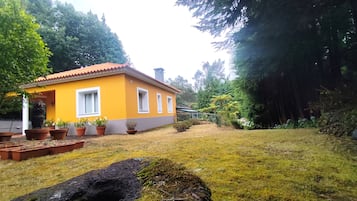 Una casa amarilla con techo rojo, rodeada de follaje y un patio cubierto de césped.