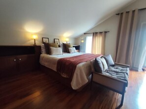 A bedroom with a large bed, bedside tables, a nightstand, a chair, and a window with curtains.