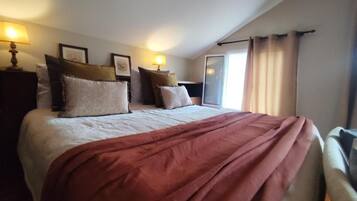 Ett hotellrum med en stor säng, två sänglampor, ett fönster med gardiner och utsikt över omgivningen.