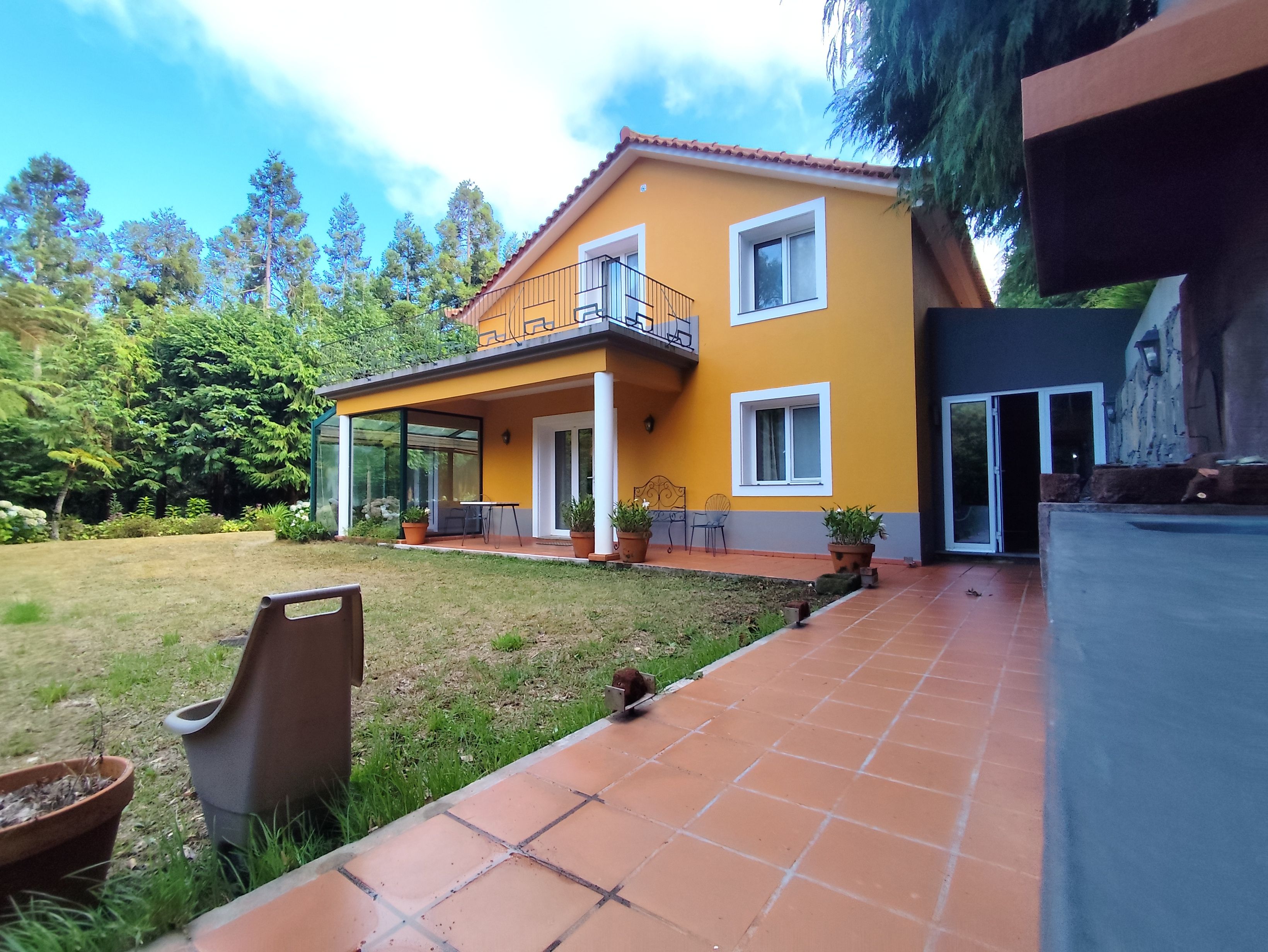 Una casa de dos pisos con fachada amarilla, un balcón y un patio cubierto.