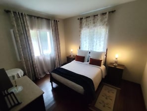 A bedroom with a bed, bedside tables, a desk, and curtains.
