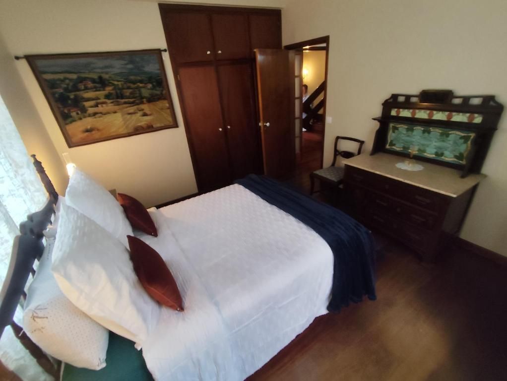 A bedroom with a bed, a dresser, a painting, and a staircase.