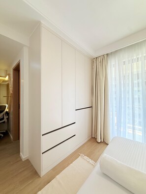 Une chambre d’hôtel comprenant un grand placard, un lit, un bureau avec une chaise et une fenêtre avec des rideaux.