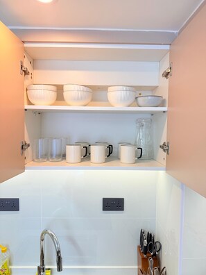 A kitchen with white cabinets, a stainless steel faucet, and various kitchenware including bowls and mugs. - 2-Bedroom Westlands Two Balconies Next To Foodplus And Artcaffe Rhapta Road (Nairobi)
