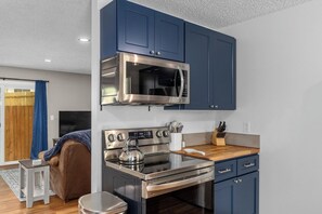 Eine kompakte Küche mit Mikrowelle, Herd und Backofen. Es gibt eine Holz Arbeitsplatte und einen Wasserkocher.