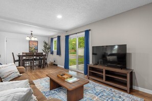 A living room with a sofa, coffee table, TV stand, and a dining area with chairs and a table. - 4 min to Hospitals • Modern 2 BR Stay (Billings)