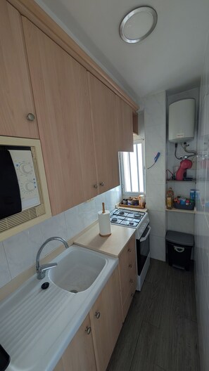 A kitchen with wooden cabinets, a gas stove, a sink, and a window providing natural light. - 3 minutes from the beach—everything is within walking distance (Grau i Platja)