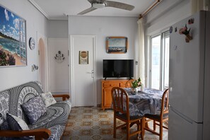 A living room with a sofa, a dining table with chairs, a television, and a ceiling fan. - 3 minutes from the beach—everything is within walking distance (Grau i Platja)