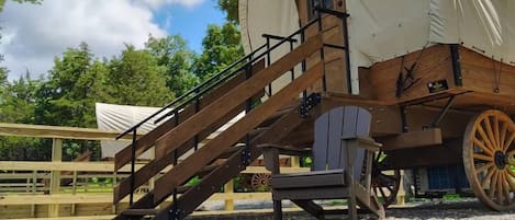 Une structure en bois couverte, avec une rampe menant à une porte, un banc en bois et une grande roue en bois.