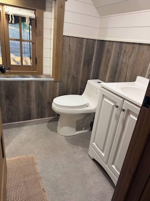 Ein Badezimmer mit einer Holzwand, einer weißen Toilette und einem weißen Waschbecken.