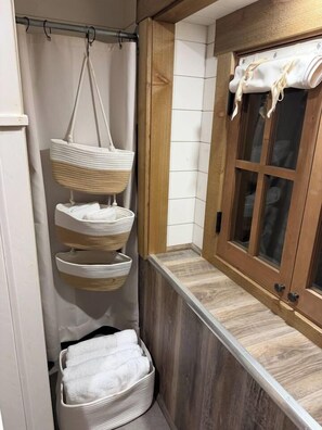 Een badkamer met een wandrek voor handdoeken, een houten bankje en een raam met een handdoek erover.