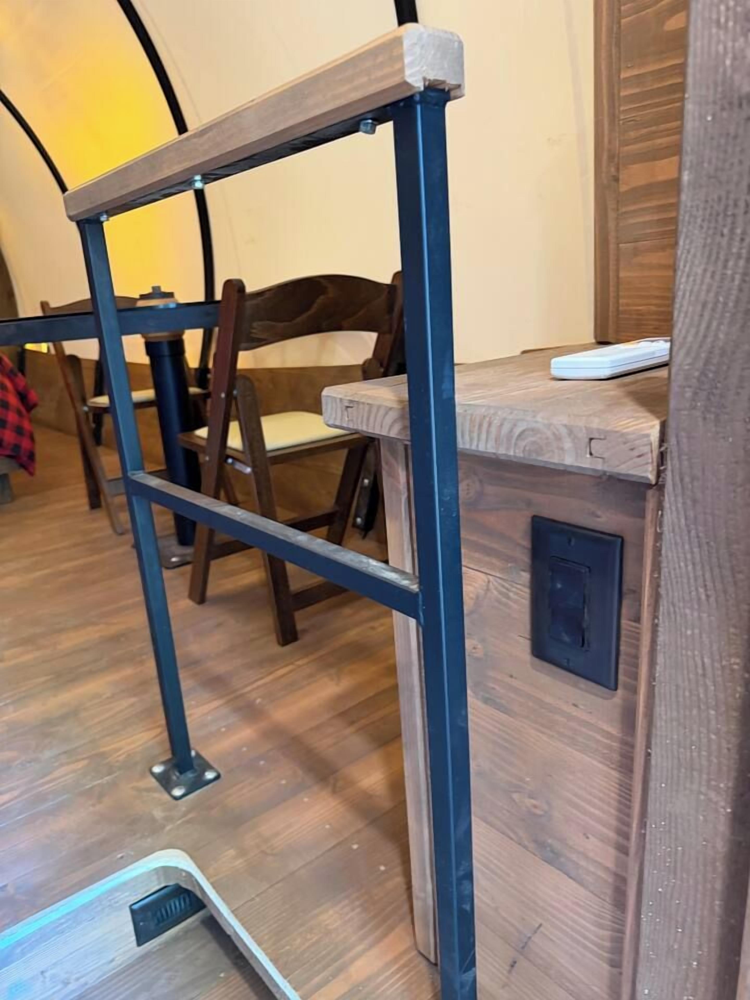 A wooden desk with a metal frame, a chair, and a power outlet on the wall.