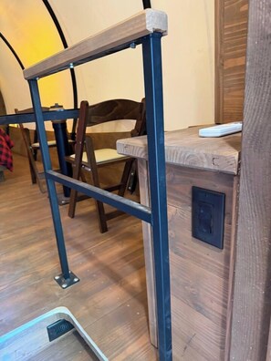 Een houten bureau met metalen frame, een stoel en een stopcontact aan de muur.
