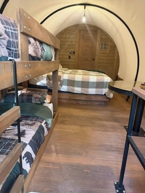Ein gemütlicher, kreisrunder Raum mit Etagenbetten und einem Einzelbett, Holzboden und einem kleinen Tisch.