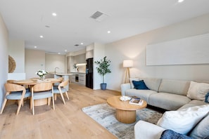 A modern living room with a sofa, coffee table, and dining area with chairs. - Spacious 3-bed Townhouse In Mile End (Adelaide)