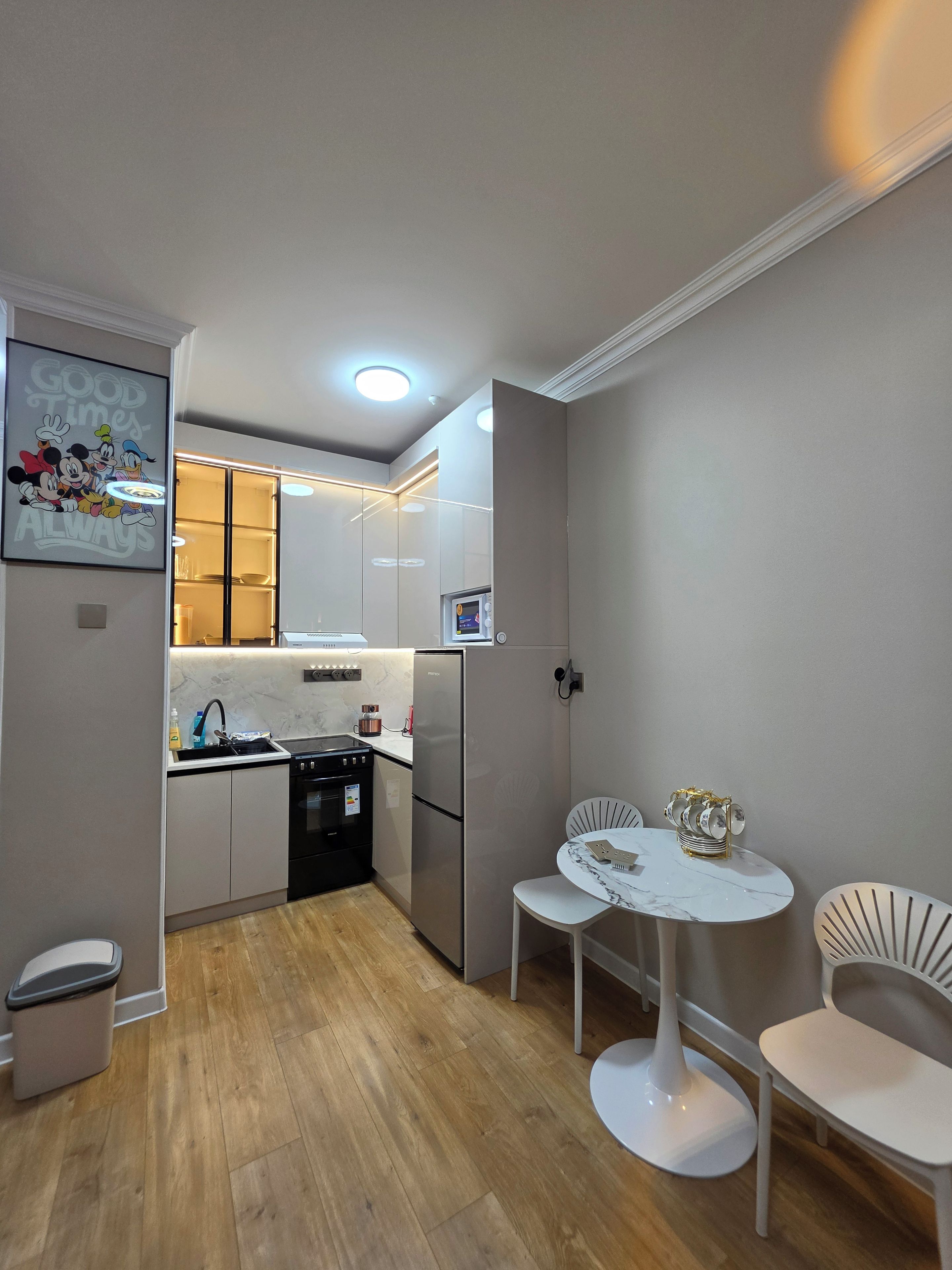 Une cuisine moderne avec un cuisinière noire, un réfrigérateur en acier inoxydable et une table à manger blanche avec deux chaises.