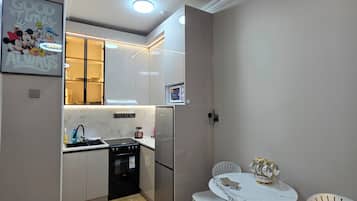 Une cuisine moderne avec un cuisinière noire, un réfrigérateur en acier inoxydable et une table à manger blanche avec deux chaises.