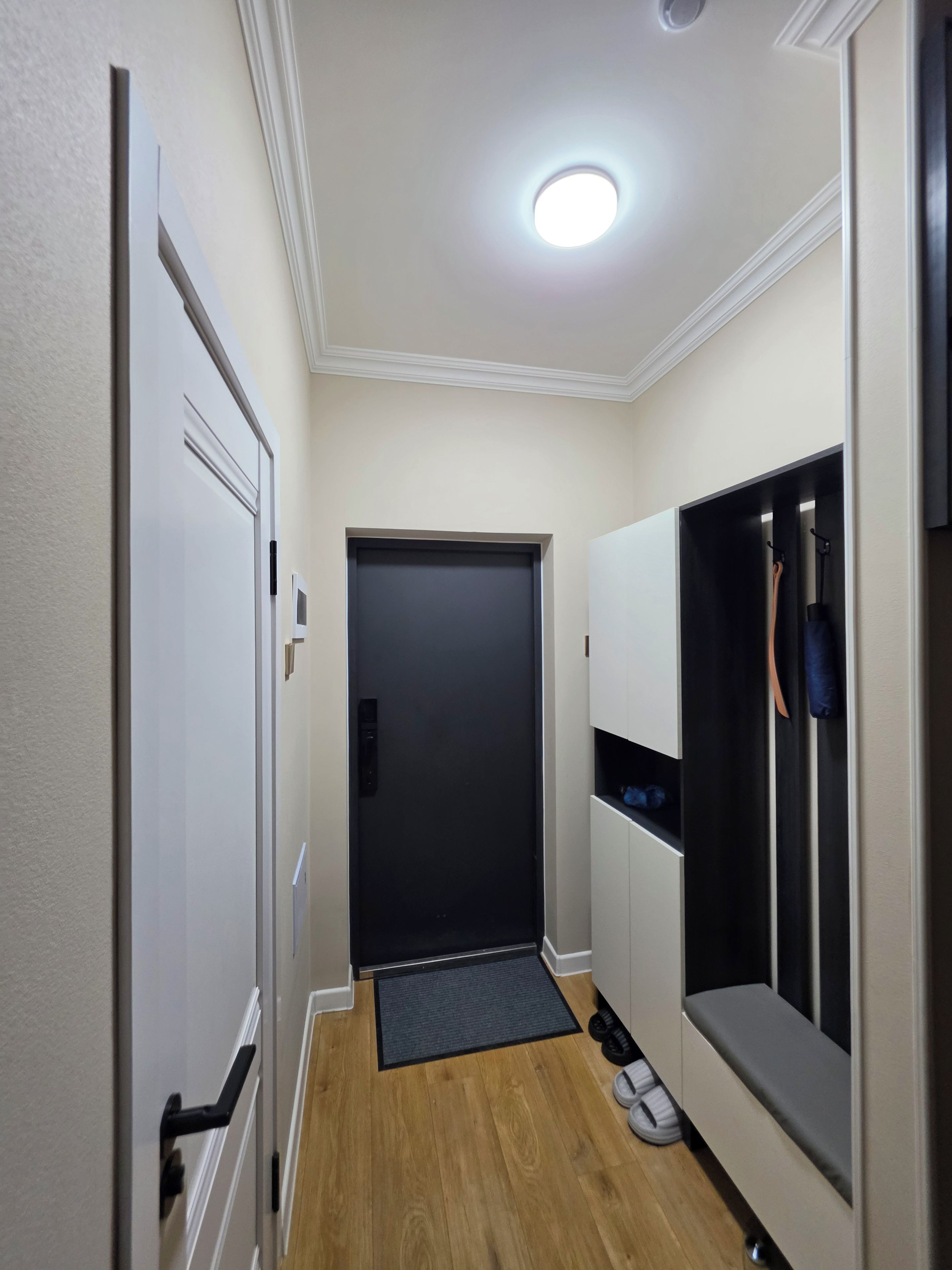 Un pasillo estrecho con una puerta al final, un perchero con objetos y un pequeño banco con zapatos.
