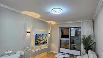 Un salon moderne doté d’un téléviseur à écran plat, d’un canapé, d’une table à manger avec des chaises et d’une grande fenêtre avec des rideaux.