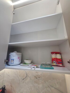 Ett köksskåp med en riskokare, en skål, ett paket barnmat och ett paket blöjor.