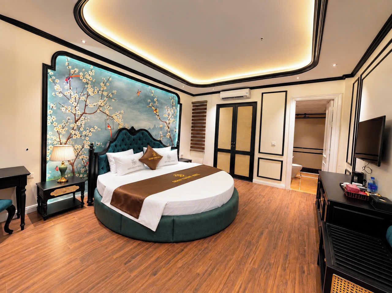 A modern hotel room with a round bed, a large wall mural, a flat-screen TV, and a wooden floor.